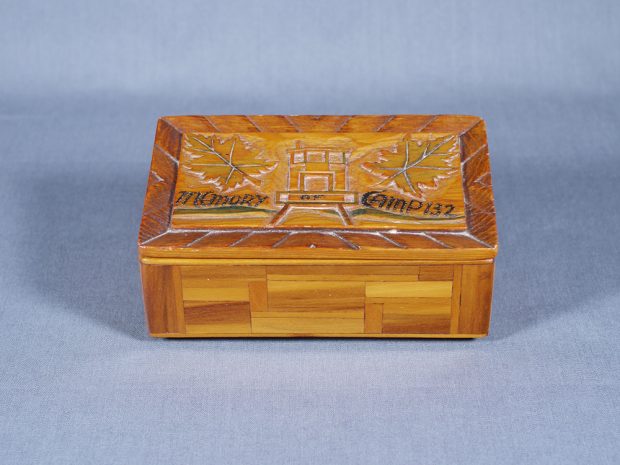 Petite boîte de bois faite à la main, avec couvercle sculpté montrant une maisonnette, avec une feuille d’érable de chaque côté.