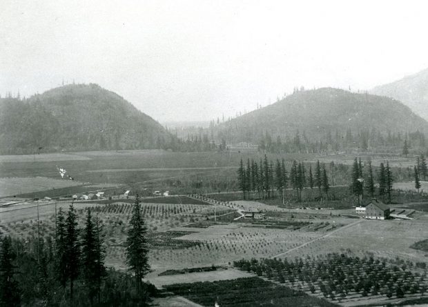 Photo en noir et blanc d'une grange, d'une maison, des champs et des montagnes en arrière-plan.