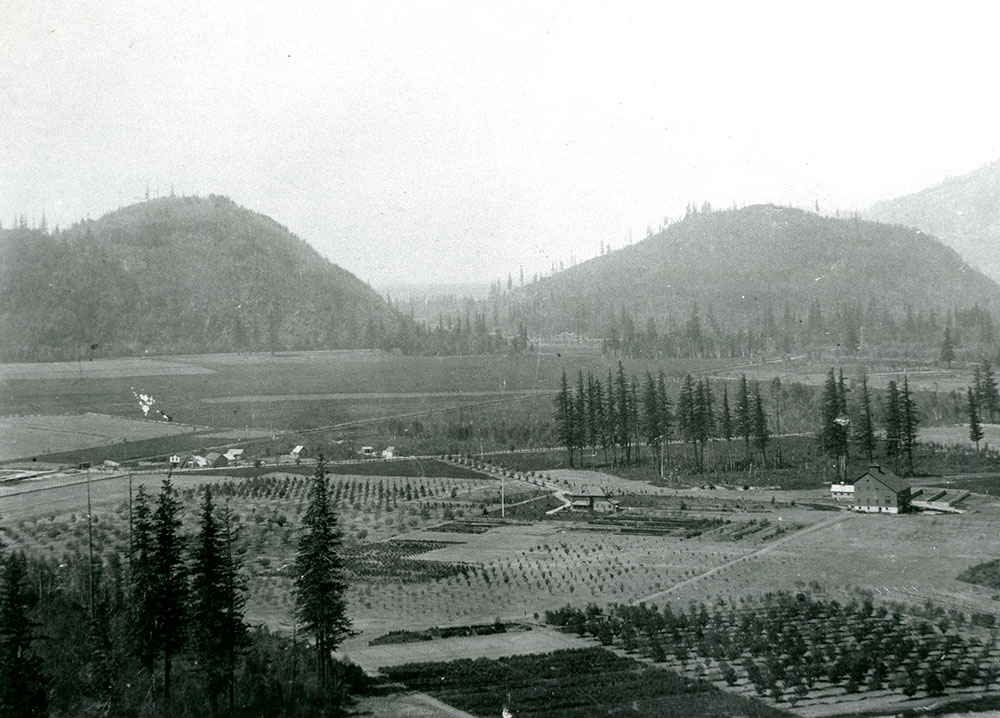 Photo en noir et blanc d'une grange, d'une maison, des champs et des montagnes en arrière-plan.