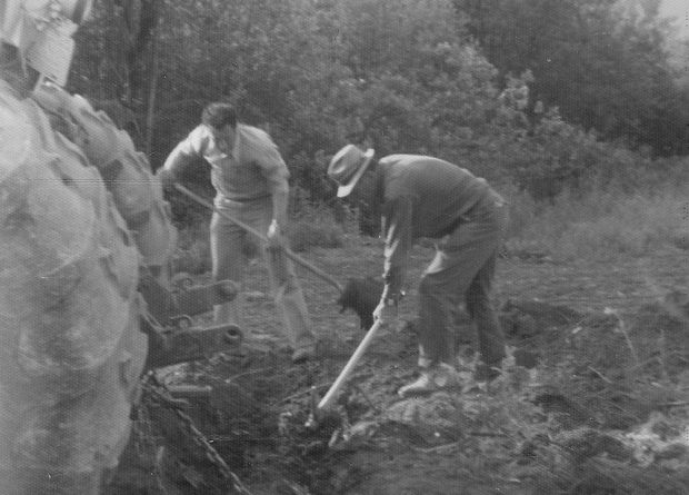 Photo en noir et blanc de deux hommes qui creusent dans le sol derrière un tracteur.