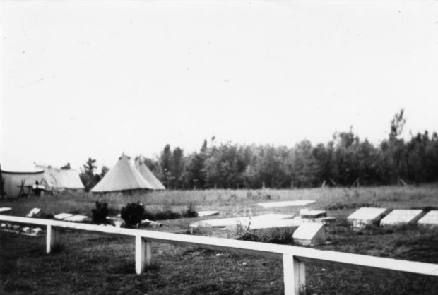 Photo en noir et blanc de tentes blanches à côté d'un cimetière.