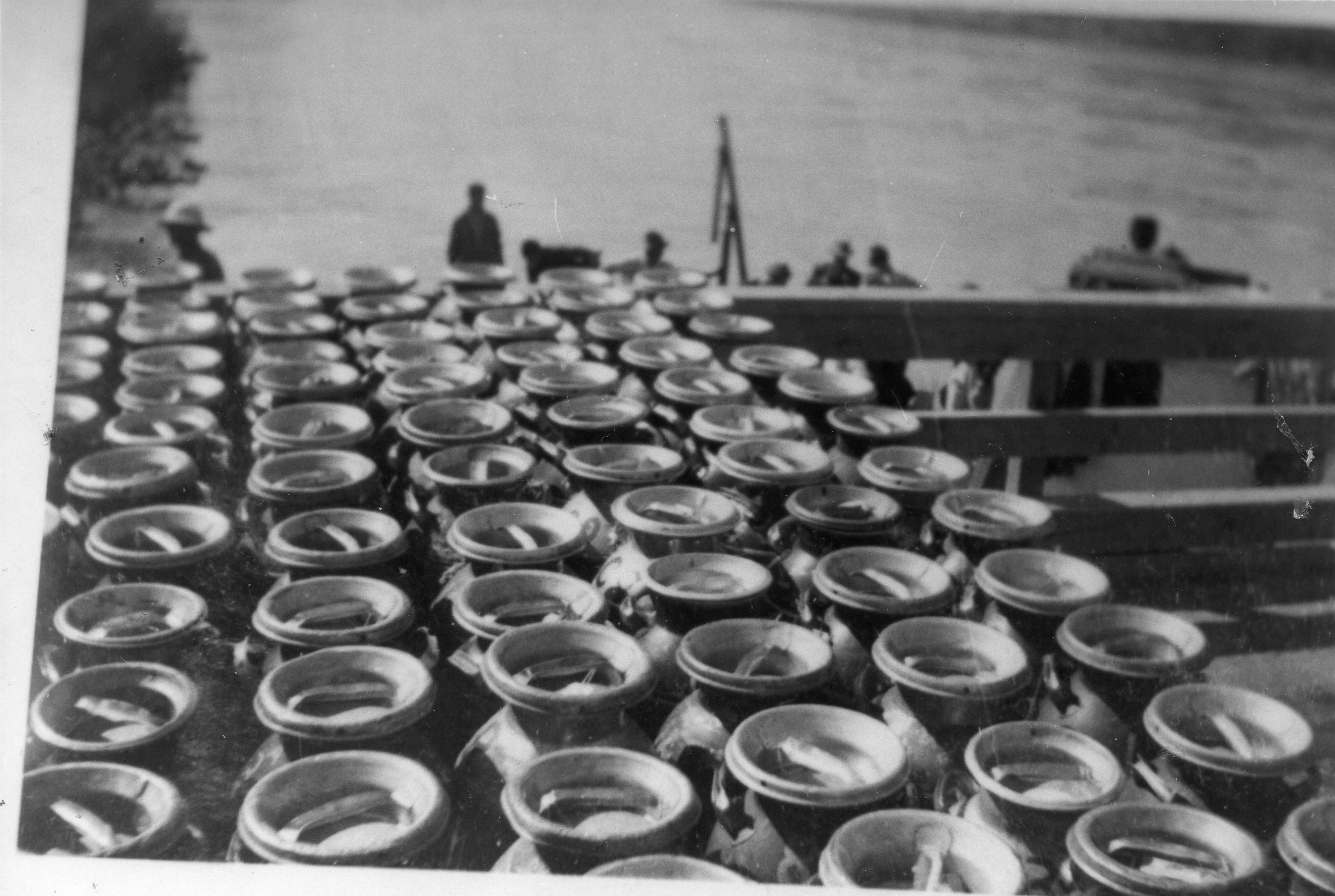 Photo en noir et blanc de bidons de lait rangés sur la plate-forme d'un camion sur le quai d'un traversier.