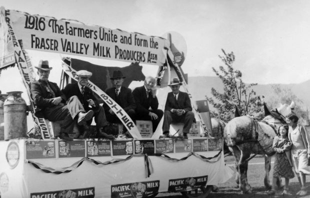 Photo en noir et blanc de cinq hommes sur un char allégorique tiré par un attelage de chevaux. Il y a une enseigne sur le char sur laquelle on peut lire « 1916 The Farmers Unite and form the Fraser Valley Milk Producers Assn » (Les fermiers s'unissent et créent la Fraser Valley Milk Producers Assn). Ils font la promotion du fromage, du beurre et du lait de la vallée du Fraser.