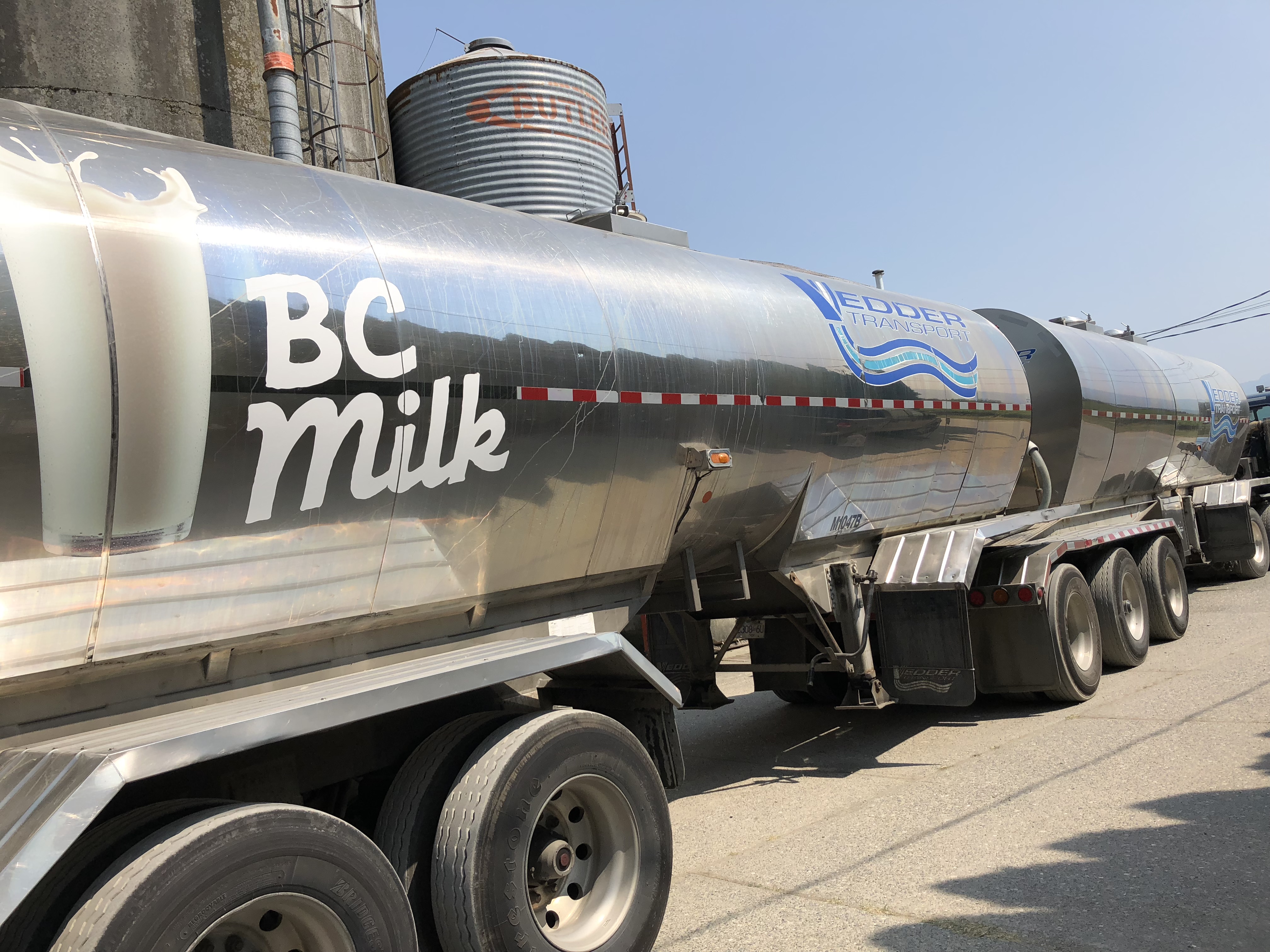 Photo en couleur d'un camion de BC Milk devant des silos. Le panneau sur le camion dit « Vedder Transport ».