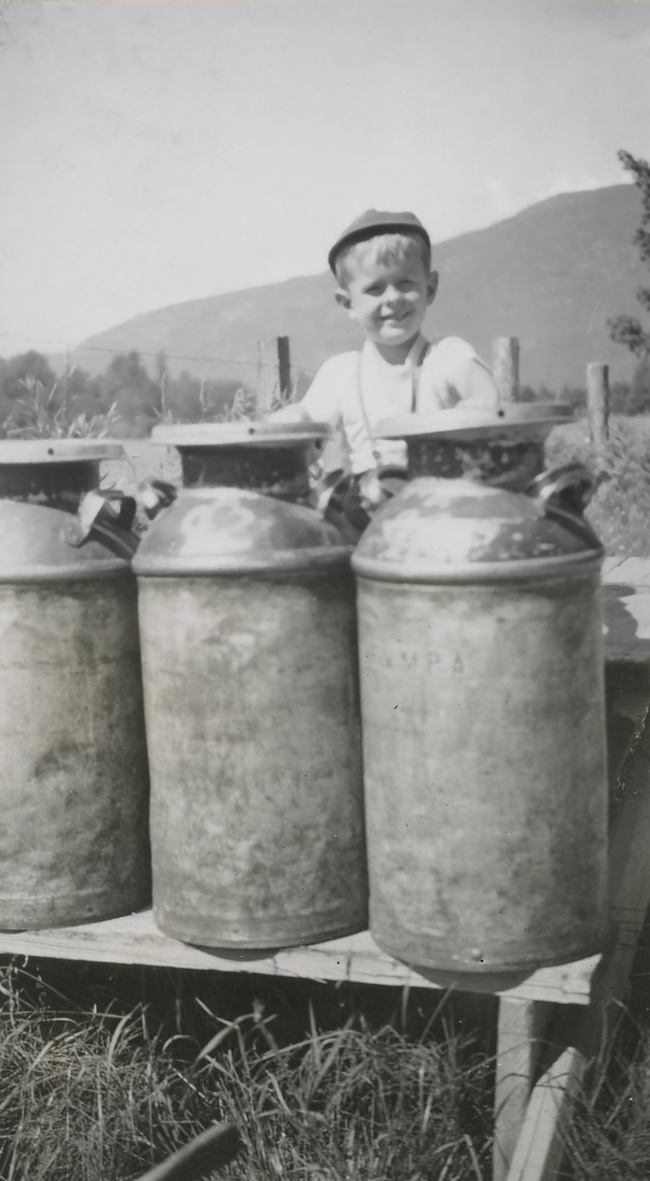 Photo en noir et blanc d'un garçon avec des bidons de lait sur un étal en bois.