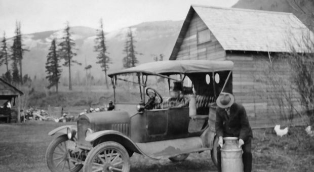 Photo en noir et blanc d'un homme chargeant des bidons de lait dans sa voiture modèle T.