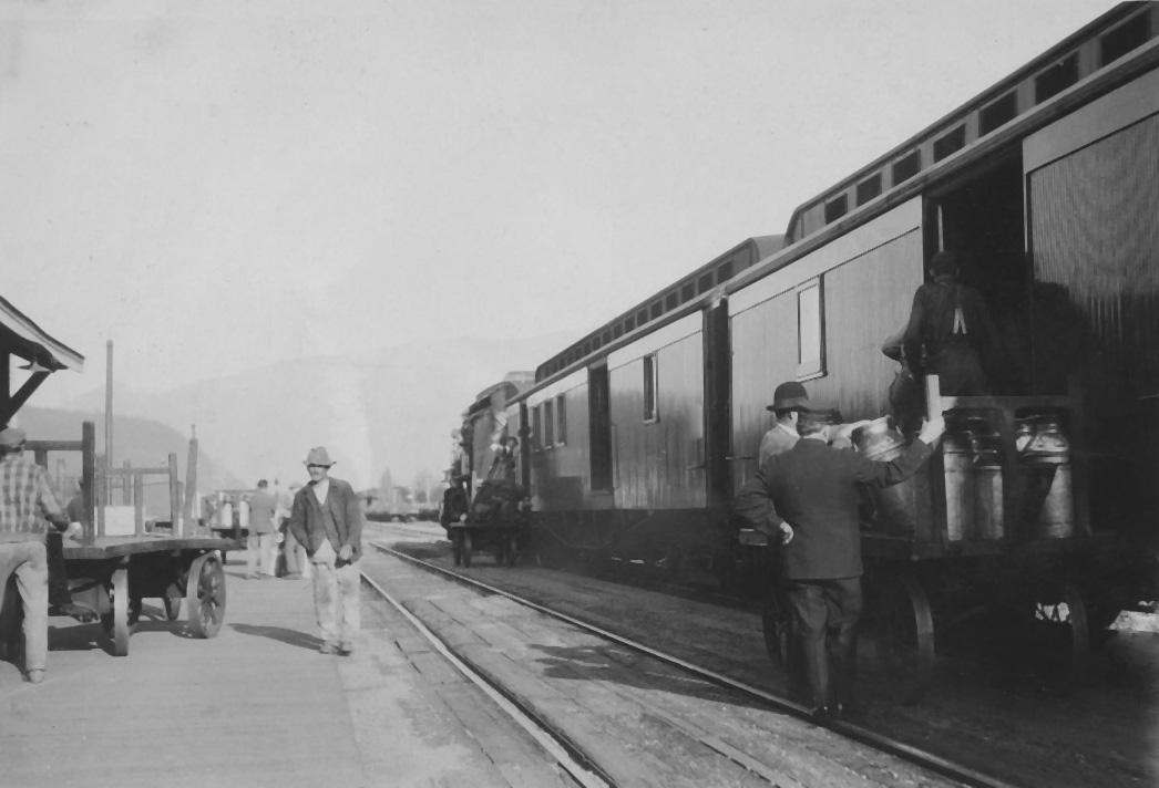 Photo en noir et blanc montrant des hommes qui chargent des bidons de lait dans un train.