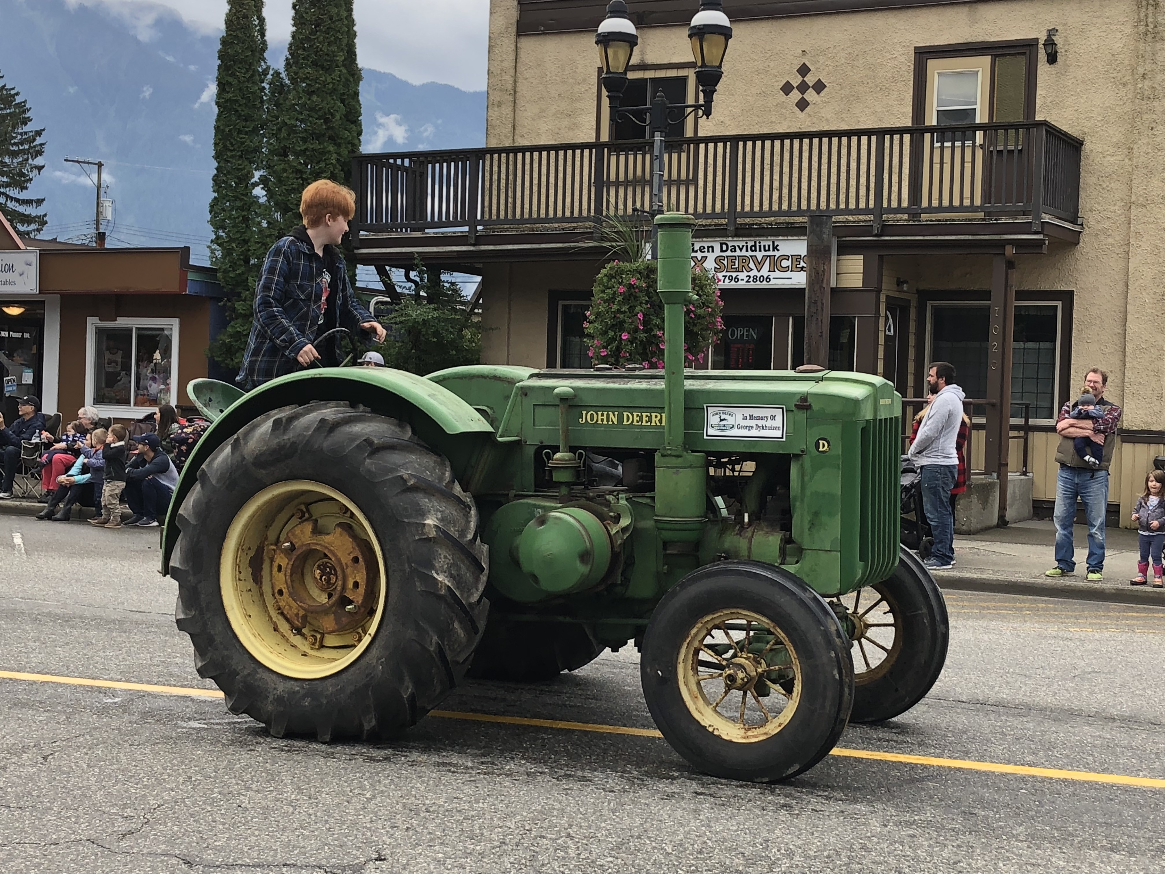 Photo en couleur d'un adolescent portant une veste à carreaux au volant d'un vieux tracteur John Deere lors d'un défilé.