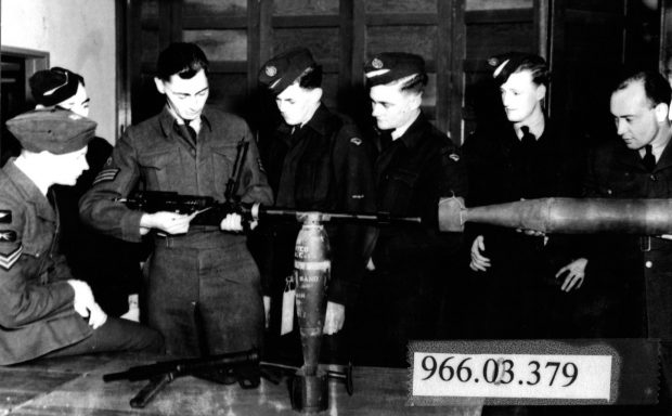 Groupe d’hommes en uniforme militaire à côté d’un instructeur montrant le fonctionnement d’une mitrailleuse antiaérienne