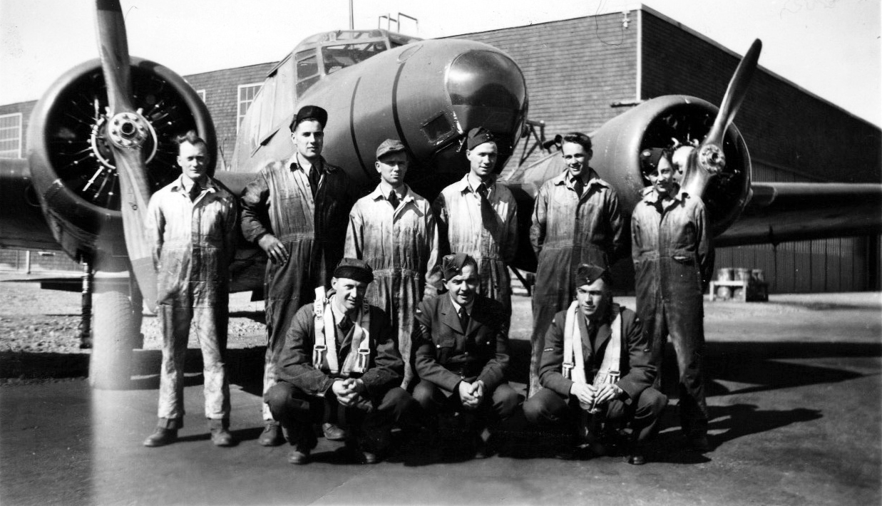 3 aviateurs et 6 mécaniciens devant un avion et un hangar