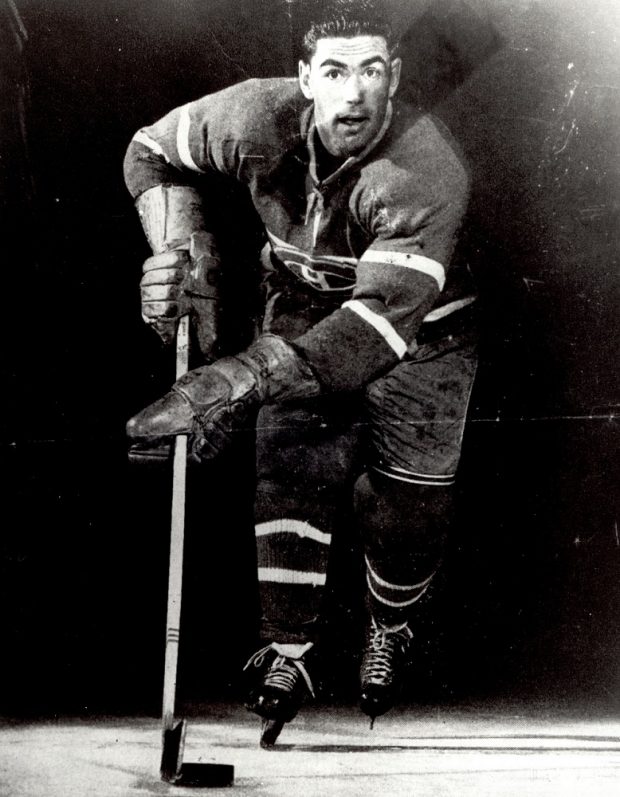 Photographie en noir et blanc d’un joueur de hockey portant le costume officiel des Canadiens de Montréal. On le voit de face avec son équipement en train de patiner.
