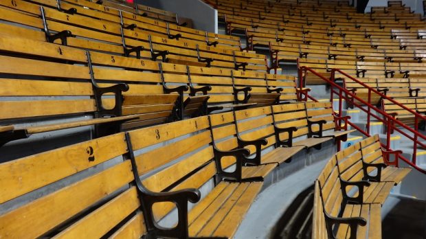 Photographie en couleurs montrant en plan rapproché des gradins intérieurs. De couleur brun pâle, les bancs peuvent accueillir deux personnes à la fois. Un accoudoir en métal noir les sépare. Les dossiers des bancs sont numérotés de 1 à 20.