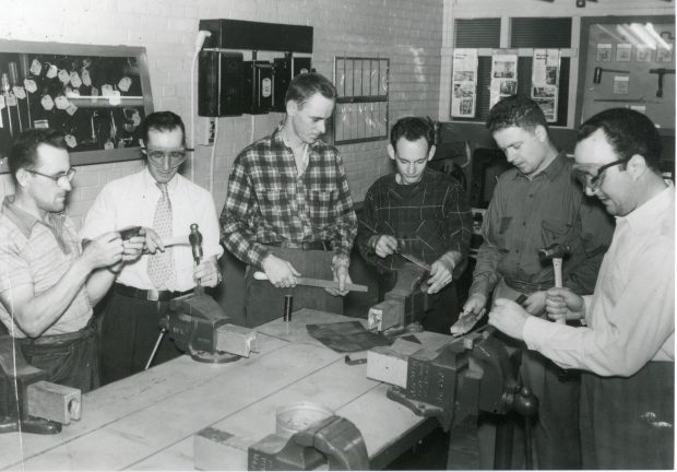 Six hommes travaillent sur un établi 