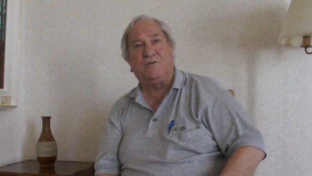 Photo de Léopold Hamel assis sur une chaise devant un mur blanc.