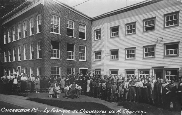 La photo montre les employés de la Fabrique de chaussures Charron rassemblés devant la manufacture. On voit qu’une nouvelle section en briques est venue remplacer la maison en bois blanche qui était érigée devant l’usine.