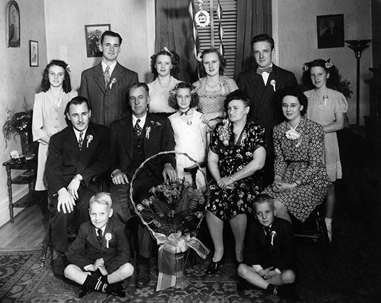 Portrait de famille montrant Léo Papin et son épouse Alice Gervais entourés de leurs 11 enfants dans le salon de leur résidence.