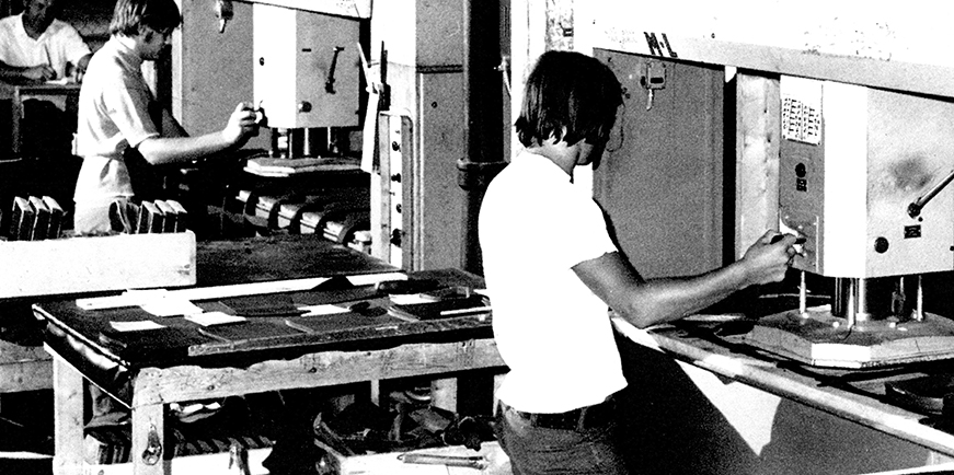 Dans cette photo, on voit deux travailleurs qui opèrent des presses à découper. Il s’agit de Marcel Gagné à gauche et Martial Gervais à droite. Au fond à gauche, on aperçoit Gilles Tétreault, contremaître du département du taillage, assis à son bureau.  