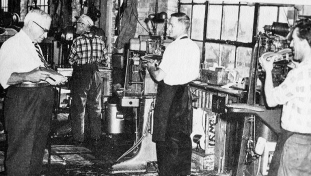La photo montre Henri Bergeron, gérant des opérations chez Lafayette de 1945 à 1960, qui inspecte une chaussure en fabrication à l’étape du montage. Trois ouvriers, Jos Geoffrion, Jean-Paul Piché et Maurice Beauregard, sont installés devant leur machine.