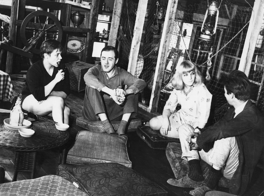 Photo noir et blanc de Raymond Lévesque et trois autres personnes assises sur des coussins dans La Butte.