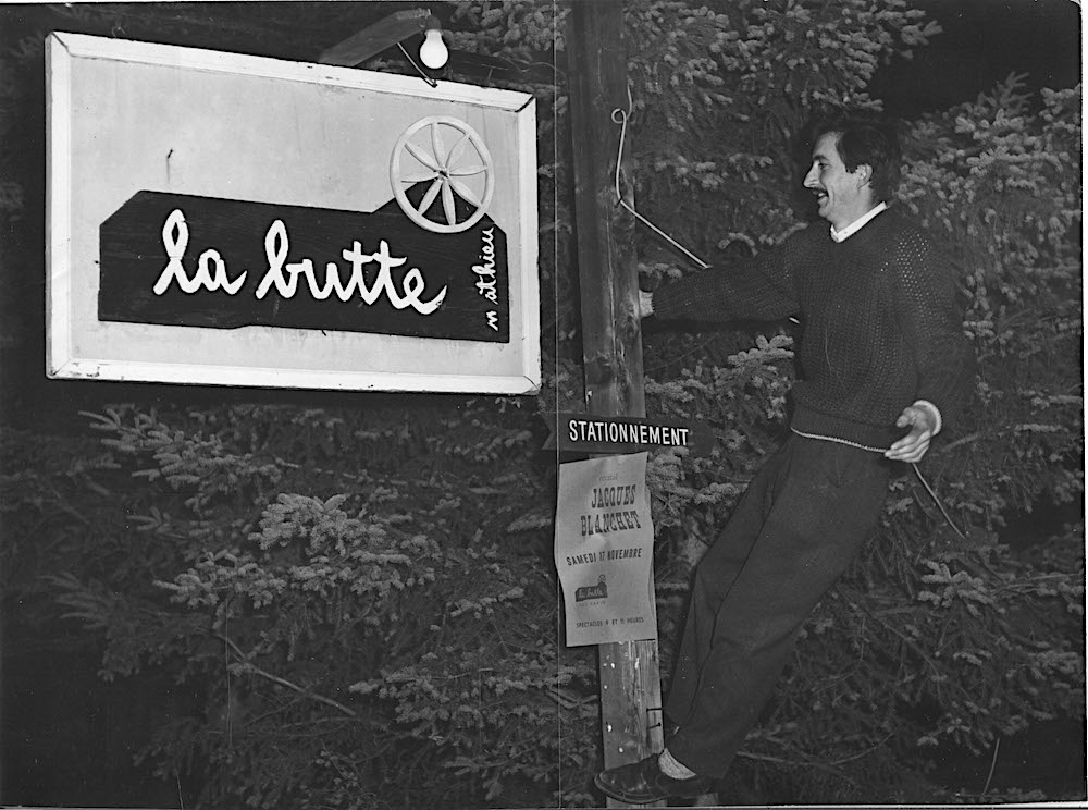 Black and white photo of Gilles Mathieu climbing a pole and installing a La Butte sign.