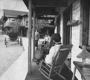 Photo noir et blanc de trois personnes assises sur la galerie d’une maison à La Butte.