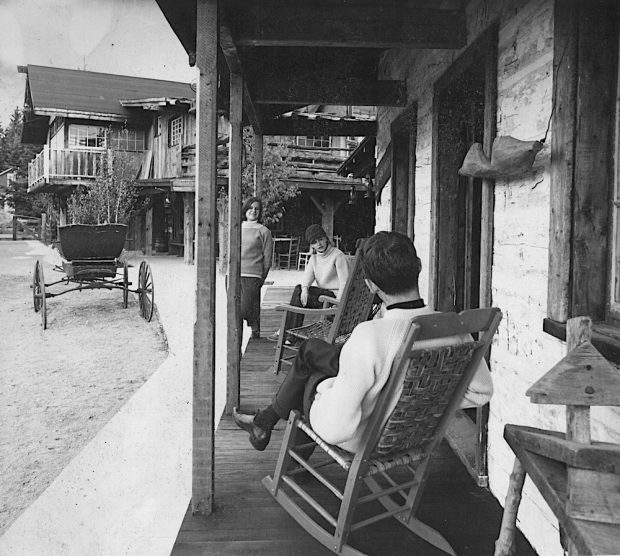 Photo noir et blanc de trois personnes assises sur la galerie d’une maison à La Butte.