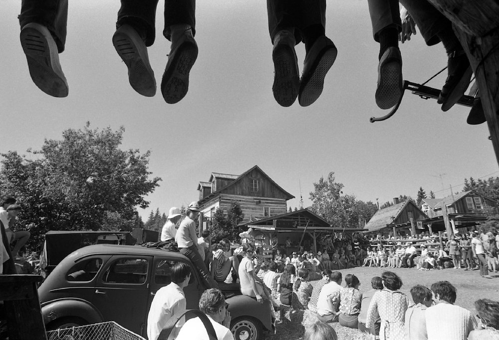 Photo noir et blanc d’une centaine de spectateurs assistant à une prestation extérieure à La Butte. Le haut de l’image montre les pieds de personnes installées sur une partie de la toiture de la Butte.