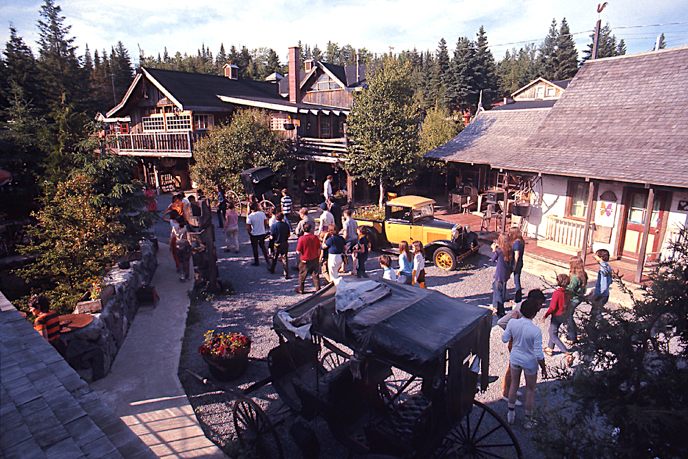 Colour photo of the exterior of La Butte à Mathieu. Several buildings provide accommodation for tourists. A carriage is installed in the middle of a walkway.