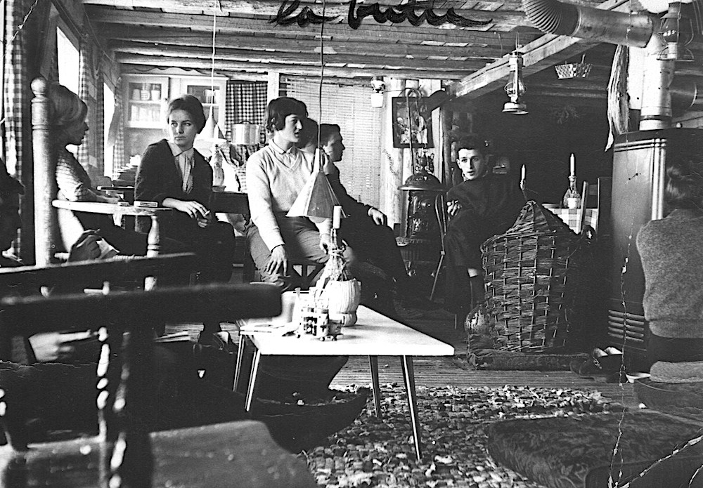 Photo noir et blanc d’une demi-douzaine de clients assis dans la première Butte. Une chandelle plantée dans le goulot d’une bouteille de Chianti trône sur une table basse. Les poutres sont apparentes.