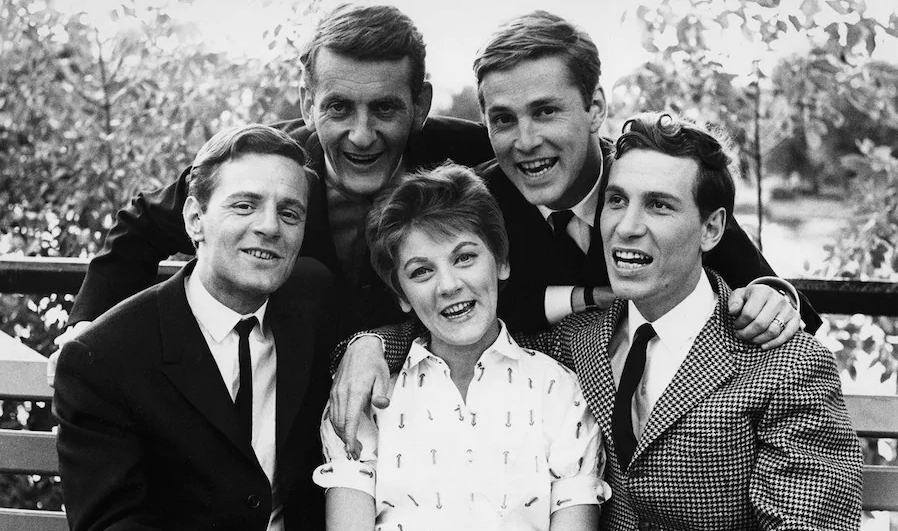 Black and white photo of the members of the group Les Bozos: Claude Léveillée, Clémence Desrochers, Jean-Pierre Ferland, Jacques Blanchet and Hervé Brousseau. The men are in full ties and Clémence Desrochers are wearing a printed blouse. They are smiling and looking happy.