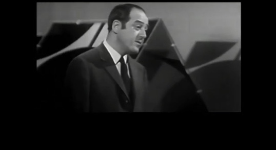Photo noir et blanc de Raymond Lévesque en complet veston lors d'un passage à une émission de télévision.