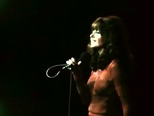 Photo couleur de Pauline Julien en robe rouge chantant en tenant un micro.