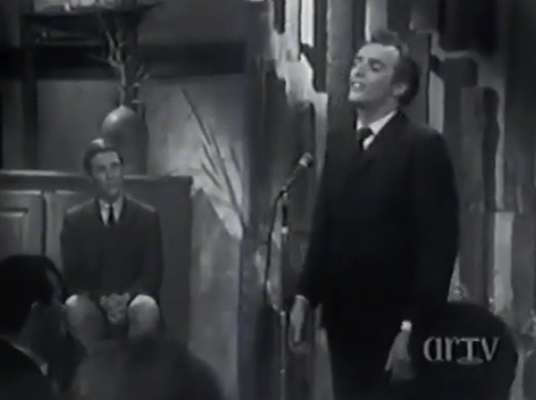 Photo noir et blanc de Gilles Vigneault chantant. Jean-Pierre Ferland est assis à l'arrière-plan.