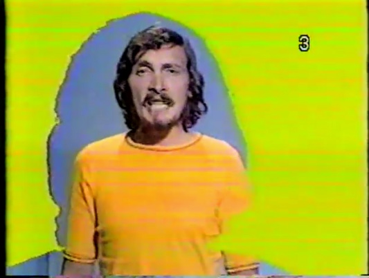 Photo couleur de Jacques Michel chantant en chandail jaune.