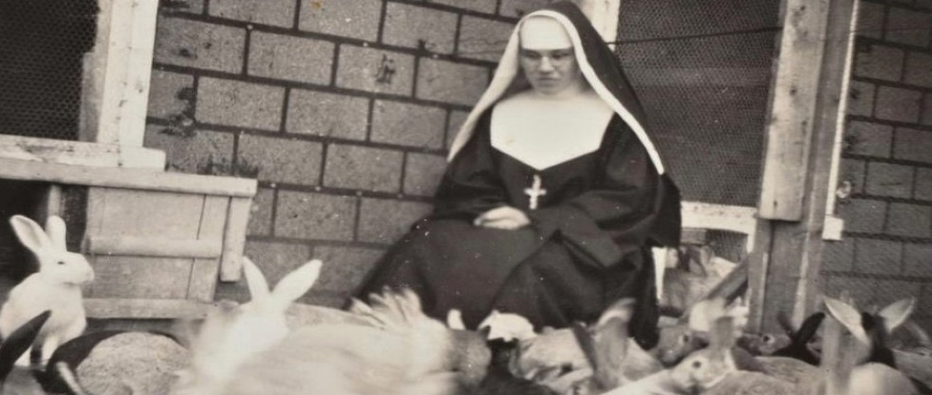 Photo en noir et blanc d’une religieuse assise avec des lapins.