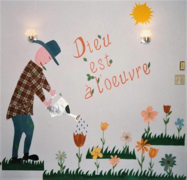 Peinture sur un mur blanc représentant une personne arrosant des plantes. Il y est inscrit : « Dieu est à l’œuvre ».