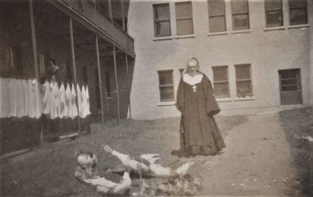 Photo dans une cour-arrière d’une sœur marchant, avec des canards et des canetons.
