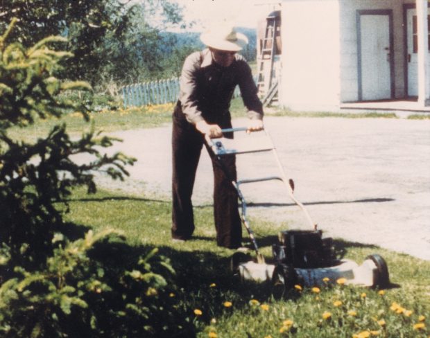 Photo en couleur d’un homme tondant le gazon avec un chapeau sur la tête.