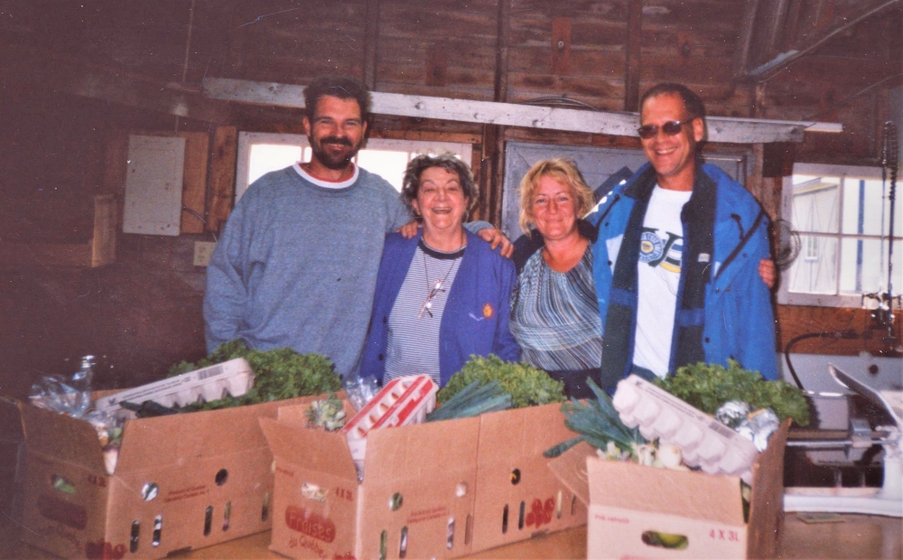 Photo en couleur de quatre employés de la ferme recevant des paniers remplis de légumes et d’œufs frais.