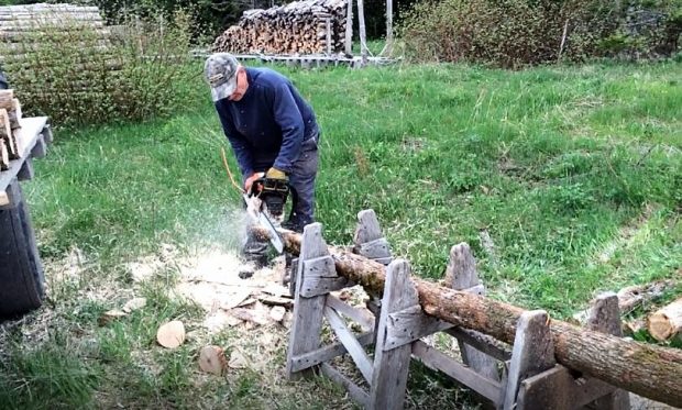 Un homme utilise une scie à chaîne pour tailler en pointe l'extrémité d'un poteau couché sur un tréteau artisanal.