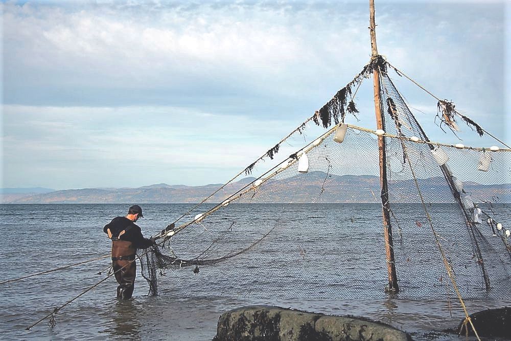 Un homme portant des bottes-pantalon est debout dans l'eau du fleuve et tient la base d'un filet de pêche attaché au sommet d’un poteau de 6 m de haut.