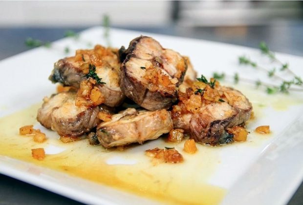 Une assiette carrée dans laquelle se trouvent des tronçons d'anguille grillés et nappés de sauce à l'écorce d'orange.