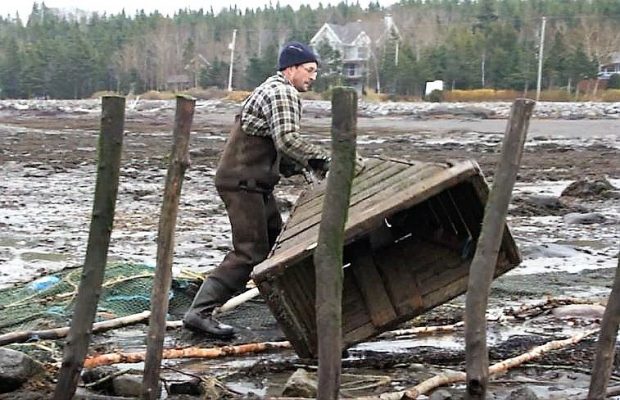 Un homme déplace un gros entonnoir en bois sur la rive du fleuve en le faisant rouler sur lui-même.
