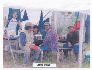 Trois hommes portant des casquettes et deux femmes à une table de pique-nique.