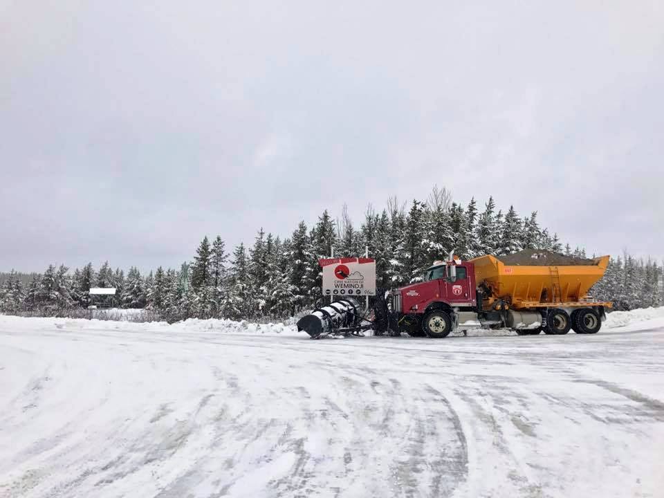 Camion rouge et jaune avec charrue et gravier sur route enneigée.