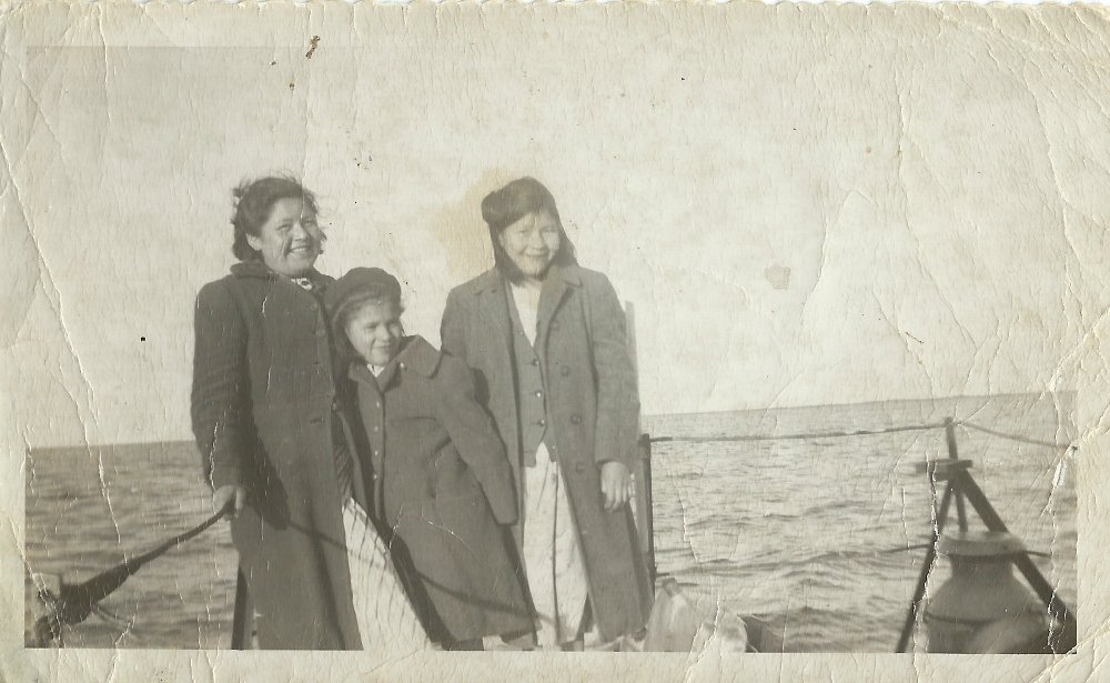 Trois filles se tiennent ensemble à l’arrière d’un bateau.