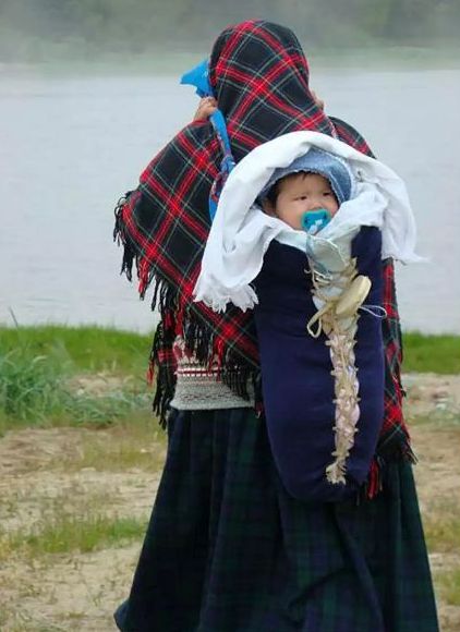 Une femme avec un châle porte son bébé sur le dos.