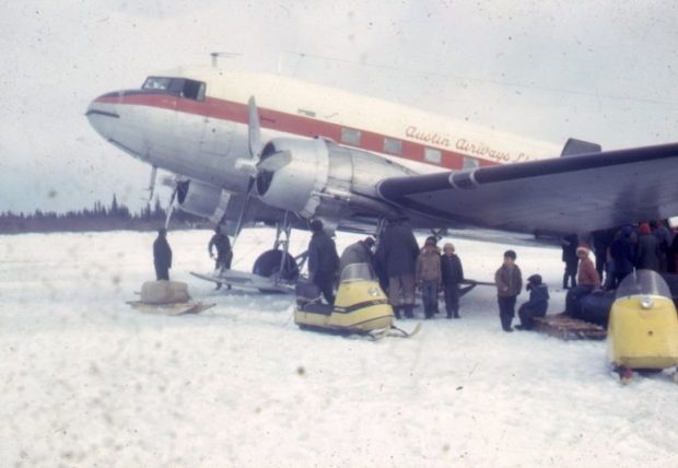 Avion propulseur sur la glace entouré de motoneiges, de traîneaux et d’un groupe d’hommes et d’enfants