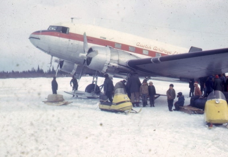 Avion propulseur sur la glace entouré de motoneiges, de traîneaux et d’un groupe d’hommes et d’enfants