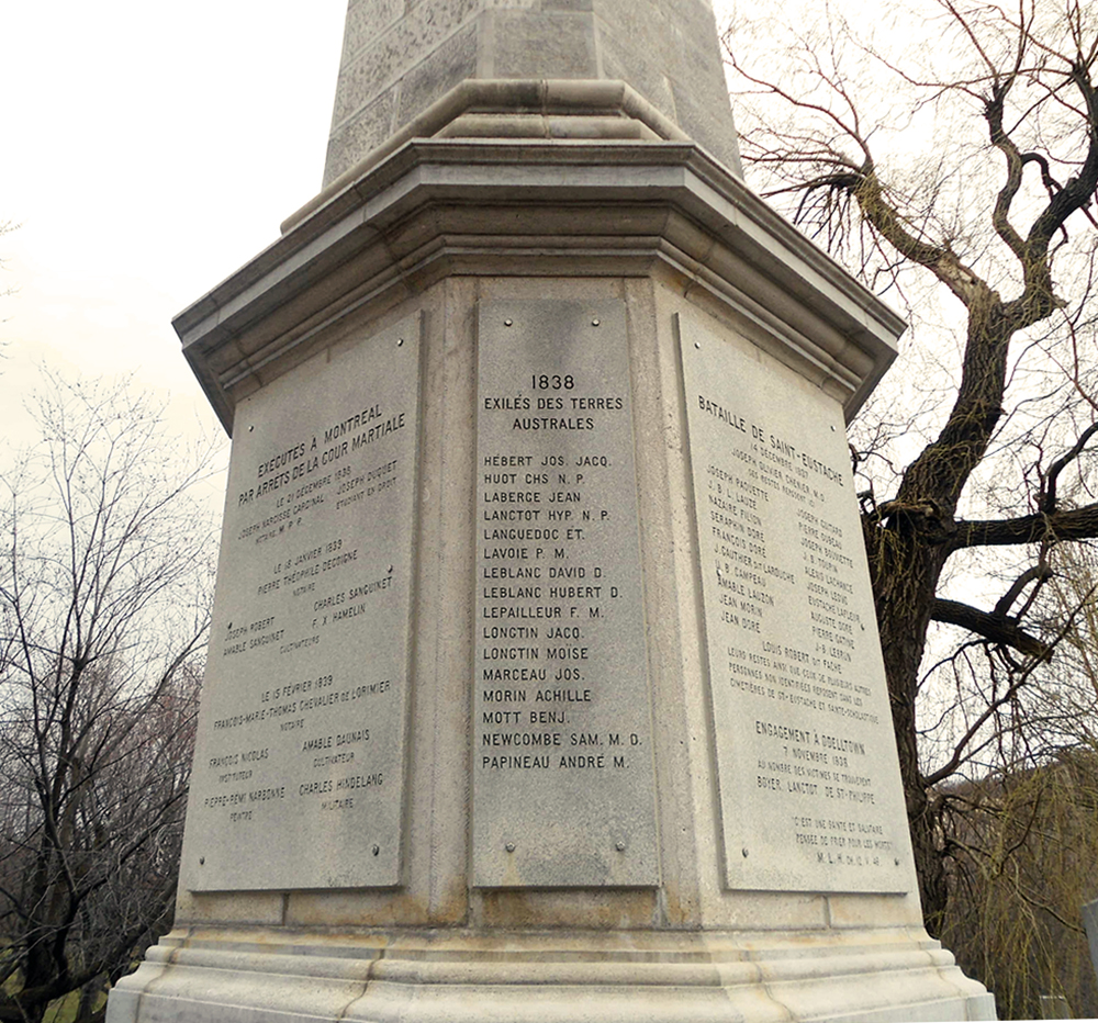 Photographie d'un monument de pierre dédié aux patriotes. Il est entouré d'arbres sans feuilles..